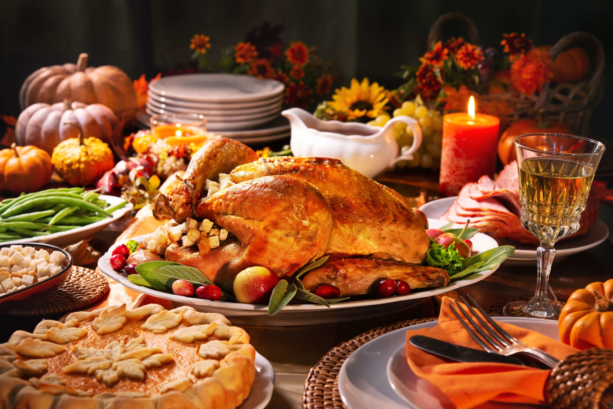 Thanksgiving dinner. Roasted turkey garnished with cranberries on a rustic style table decoraded with pumpkins, vegetables, pie, flowers and candles